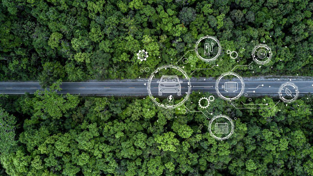 Vogelansicht einer geraden Straße die durch einen grünen Wald führt. Auf dem Bild sind weiße Zeichnungen, die das Konzept E-auto symbolisieren.